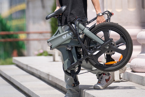 Uomo che porta bici elettrica pieghevole DYU T1 grigia su scale. Uomo che porta bici elettrica pieghevole DYU T1 grigia su scale.