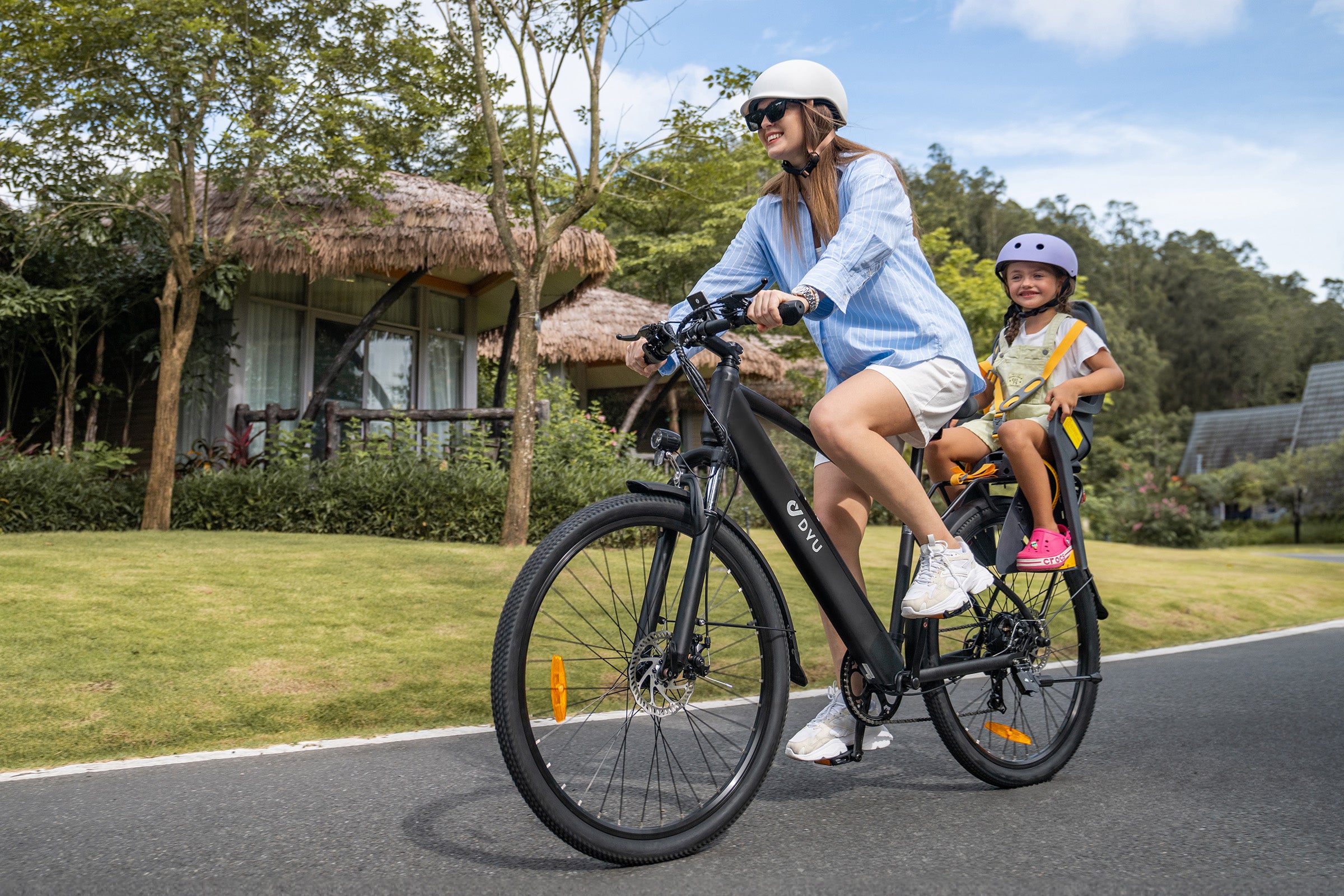 Donna in bicicletta elettrica DYU C5 nera con bambino nel seggiolino, in ambiente urbano. Donna in bicicletta elettrica DYU C5 nera con bambino nel seggiolino, in ambiente urbano.