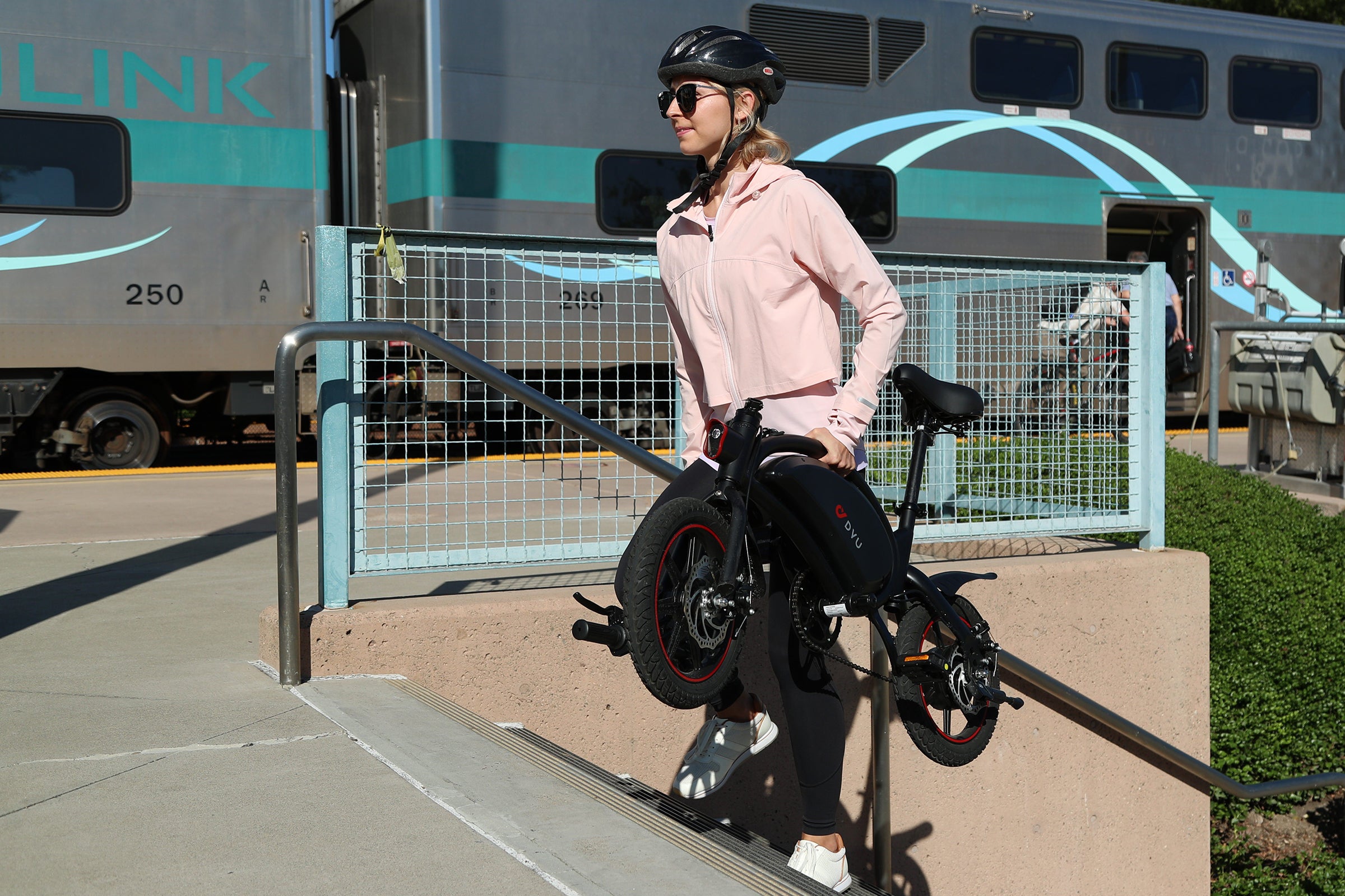 Donna con casco che porta in spalla la bici elettrica D3F nera per il trasporto urbano. Donna con casco che porta in spalla la bici elettrica D3F nera per il trasporto urbano.