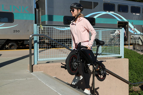 Donna con casco che porta in spalla la bici elettrica D3F nera per il trasporto urbano. Donna con casco che porta in spalla la bici elettrica D3F nera per il trasporto urbano.